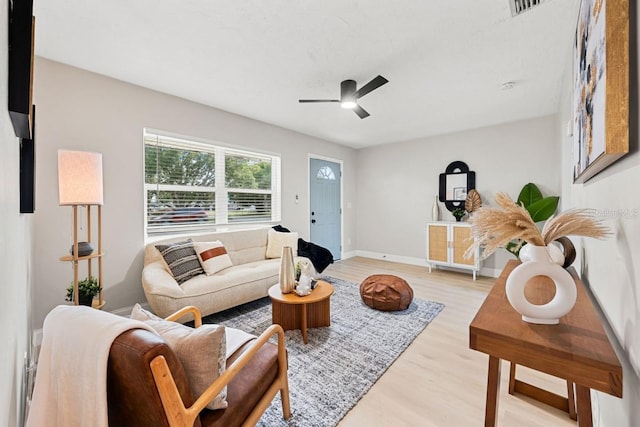 living room featuring light wood finished floors, visible vents, baseboards, and a ceiling fan