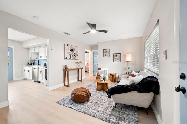 living room featuring light wood-style floors, a ceiling fan, visible vents, and baseboards