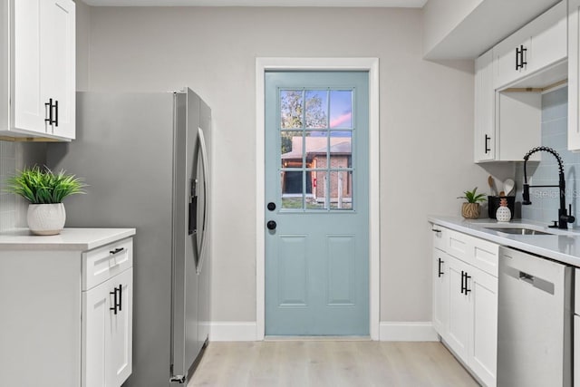 kitchen with light wood finished floors, decorative backsplash, stainless steel appliances, and a sink