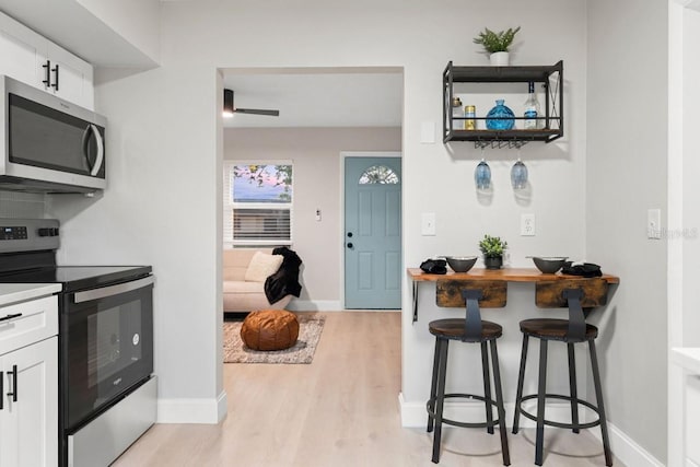 kitchen with baseboards, stainless steel appliances, white cabinets, a kitchen bar, and light wood-type flooring