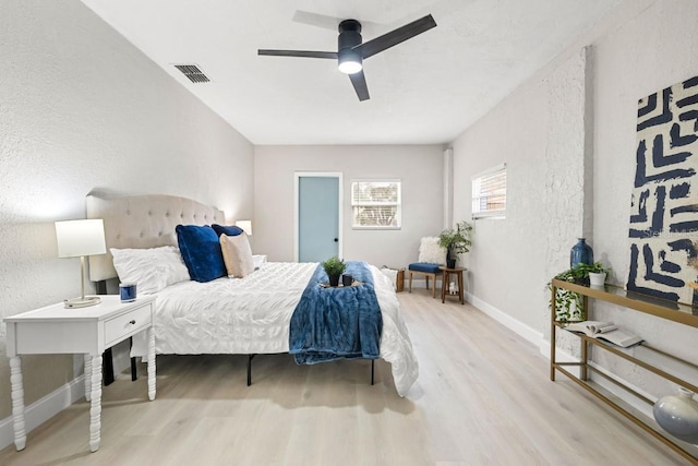 bedroom with visible vents, a ceiling fan, wood finished floors, baseboards, and a textured wall