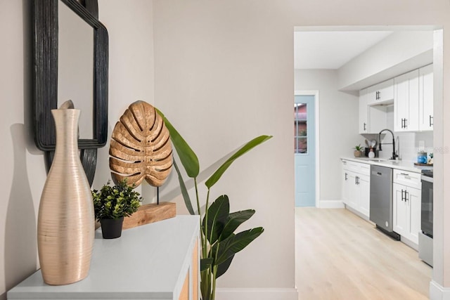 kitchen featuring dishwasher, light wood-type flooring, light countertops, white cabinets, and a sink