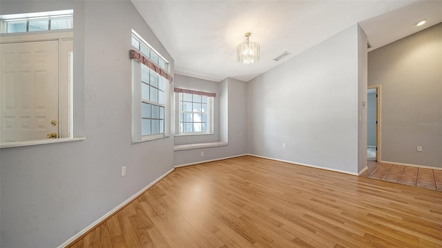 spare room with wood finished floors, visible vents, lofted ceiling, and a chandelier