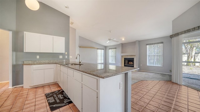 kitchen featuring ceiling fan, light tile patterned floors, a peninsula, a fireplace, and a sink