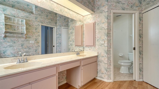 full bath featuring wood finished floors, toilet, wallpapered walls, and a sink