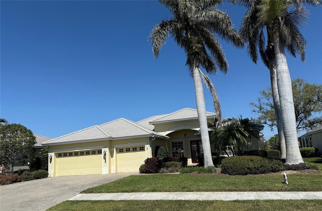 view of front facade featuring a front lawn, a tiled roof, stucco siding, driveway, and an attached garage