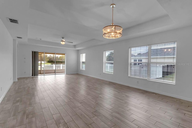 empty room featuring wood finished floors, visible vents, baseboards, a raised ceiling, and ceiling fan with notable chandelier