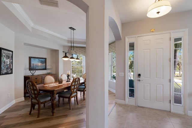 entryway with visible vents, crown molding, baseboards, arched walkways, and a raised ceiling