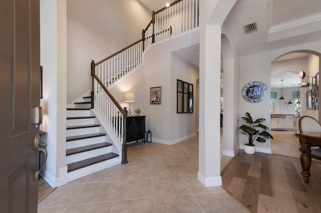 entryway featuring visible vents, baseboards, stairs, a high ceiling, and arched walkways