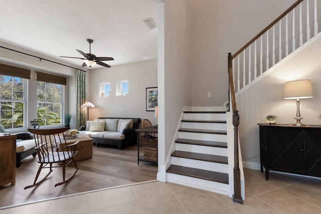 tiled living area featuring stairway, baseboards, visible vents, and ceiling fan