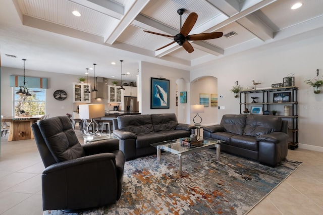 living area with ceiling fan, light tile patterned floors, beam ceiling, arched walkways, and coffered ceiling