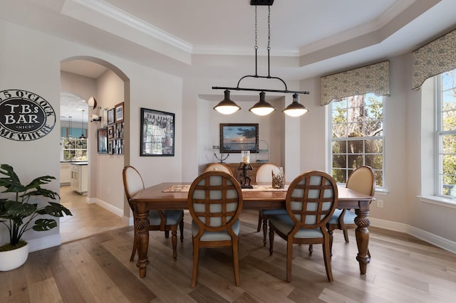 dining room featuring arched walkways, a healthy amount of sunlight, light wood finished floors, and a tray ceiling