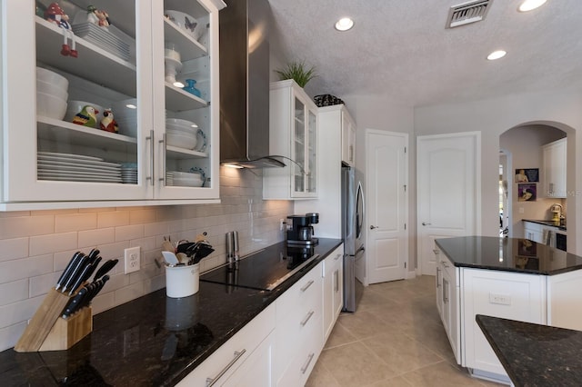 kitchen with visible vents, dark stone countertops, freestanding refrigerator, arched walkways, and wall chimney exhaust hood