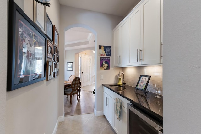 interior space with beverage cooler, decorative backsplash, arched walkways, white cabinetry, and a sink