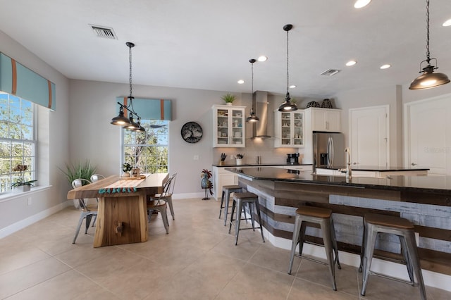 kitchen featuring dark countertops, tasteful backsplash, stainless steel fridge, a breakfast bar area, and wall chimney exhaust hood