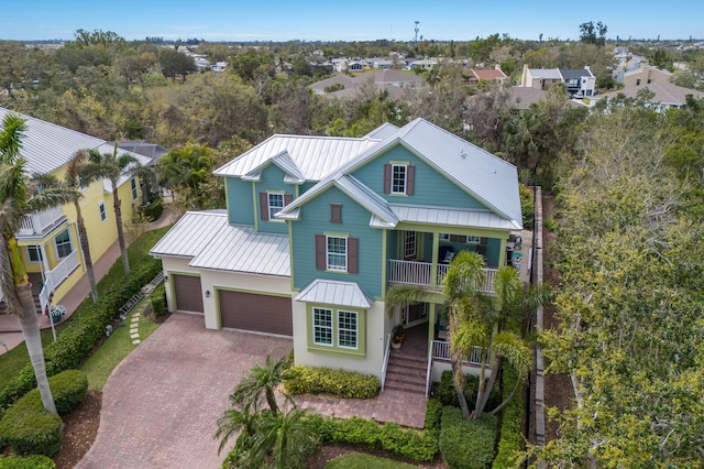 beach home with a balcony, a standing seam roof, an attached garage, decorative driveway, and metal roof