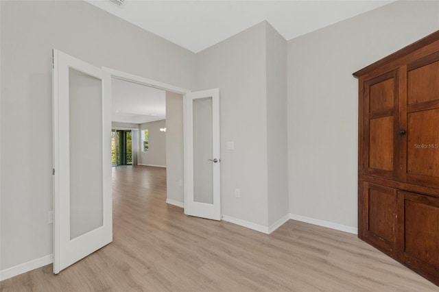 empty room with french doors, baseboards, and light wood-style floors