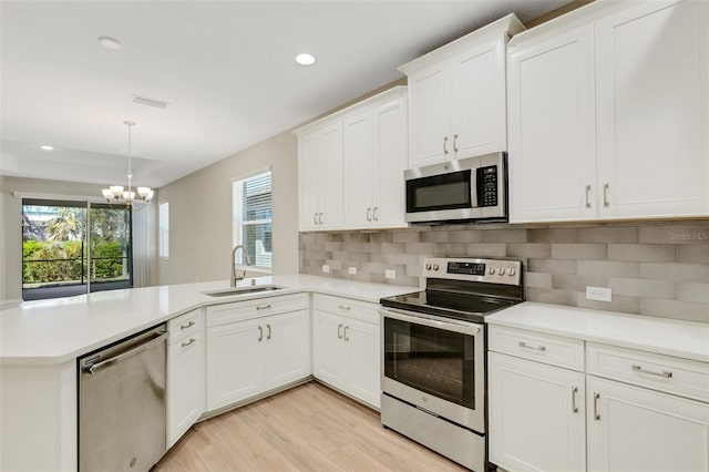 kitchen with a sink, appliances with stainless steel finishes, a peninsula, light countertops, and a chandelier