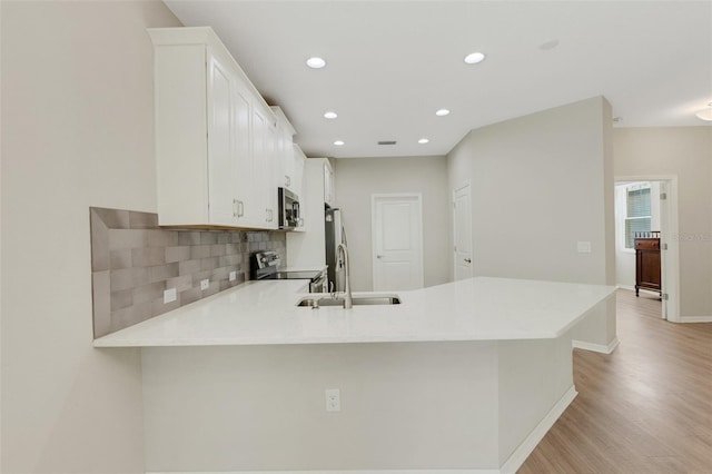 kitchen with a peninsula, light countertops, white cabinets, appliances with stainless steel finishes, and backsplash