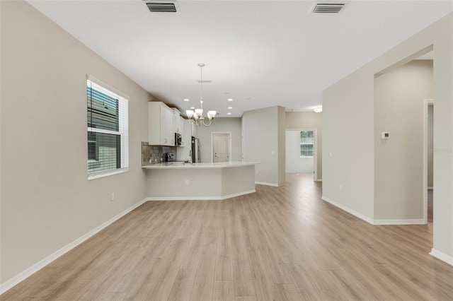 unfurnished living room featuring visible vents, light wood-style flooring, baseboards, and an inviting chandelier