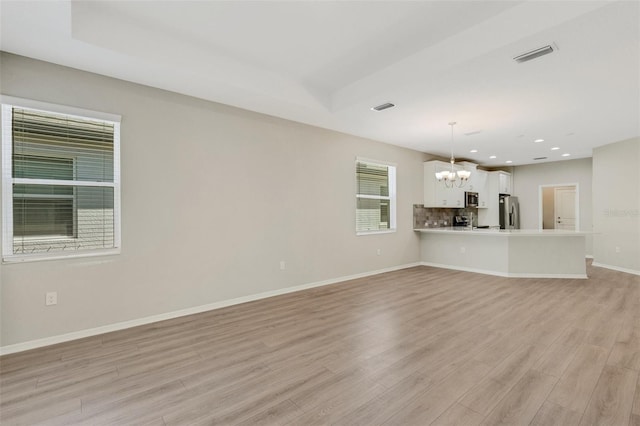 unfurnished living room with a chandelier, visible vents, baseboards, and light wood-style floors