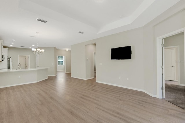 unfurnished living room with visible vents, light wood-style flooring, baseboards, and an inviting chandelier