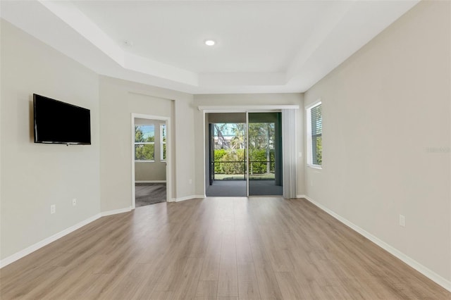 unfurnished room with plenty of natural light, baseboards, a raised ceiling, and light wood-style floors