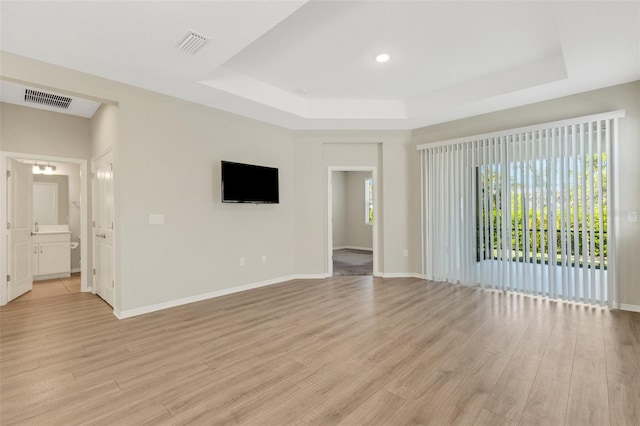 unfurnished living room with a tray ceiling, baseboards, visible vents, and light wood-type flooring