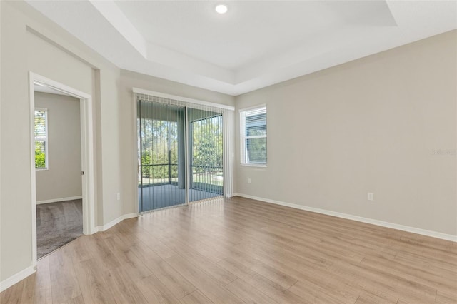 unfurnished room featuring a raised ceiling, baseboards, light wood-type flooring, and a wealth of natural light