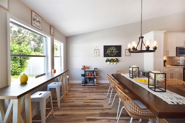 dining area featuring baseboards, vaulted ceiling, a textured ceiling, light wood-type flooring, and a chandelier