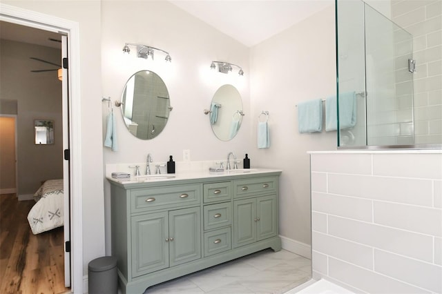 ensuite bathroom with a sink, lofted ceiling, double vanity, and a tile shower