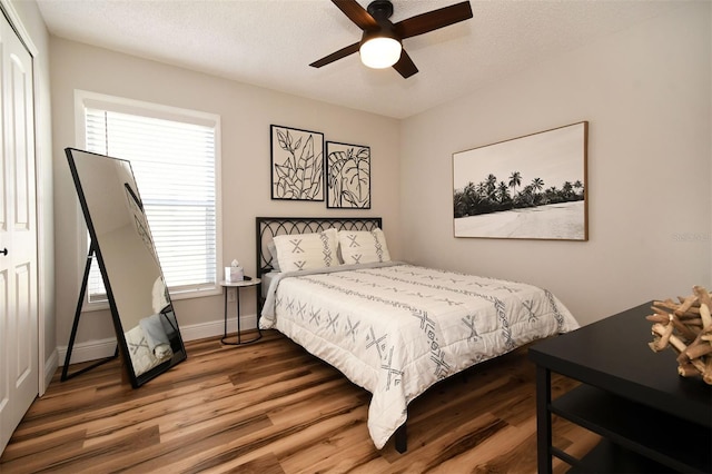 bedroom with ceiling fan, a textured ceiling, baseboards, and wood finished floors