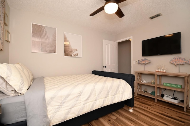 bedroom featuring visible vents, a textured ceiling, a ceiling fan, and wood finished floors