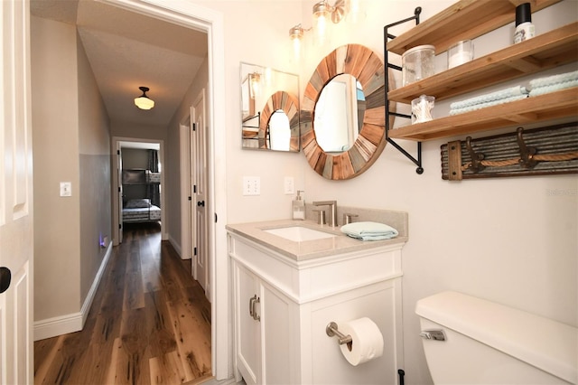 bathroom with baseboards, toilet, wood finished floors, and vanity