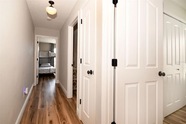 hallway with a textured ceiling, baseboards, and light wood-style floors