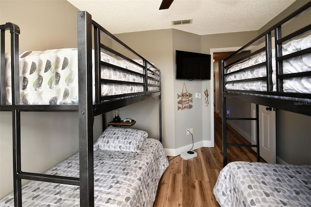 bedroom with wood finished floors, baseboards, visible vents, ceiling fan, and a textured ceiling