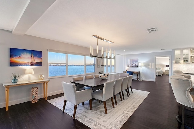 dining space featuring wood finished floors, visible vents, a water view, and baseboards