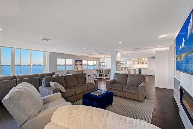 living area featuring visible vents, recessed lighting, dark wood-type flooring, a water view, and a glass covered fireplace