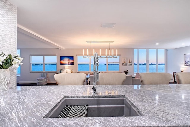 kitchen with a sink, visible vents, stone counters, and open floor plan