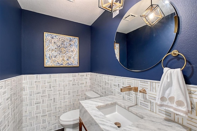 bathroom featuring tile walls, toilet, wainscoting, and a textured ceiling