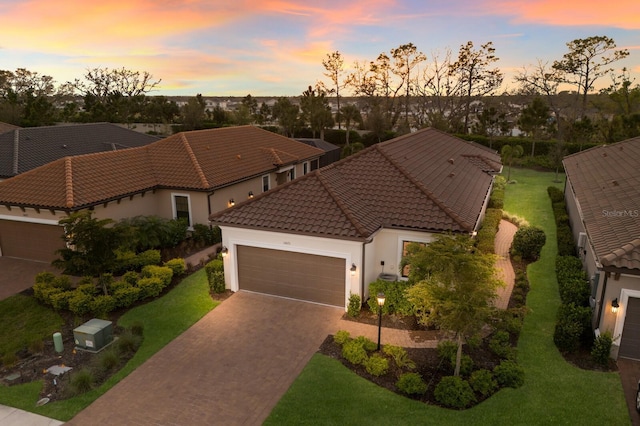 mediterranean / spanish-style home featuring an attached garage, a tile roof, stucco siding, a yard, and driveway