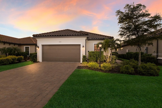 mediterranean / spanish-style house with driveway, stucco siding, a garage, a tiled roof, and a lawn