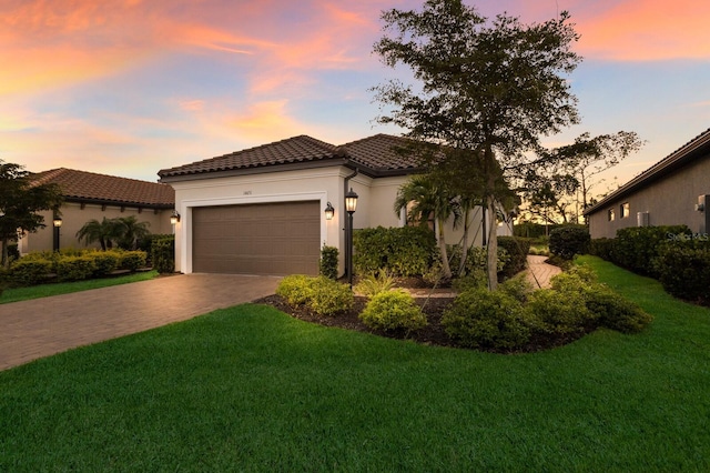 mediterranean / spanish home featuring stucco siding, a front lawn, a tile roof, decorative driveway, and a garage