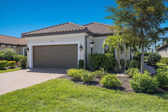 mediterranean / spanish-style home featuring a front yard, stucco siding, a garage, a tile roof, and decorative driveway