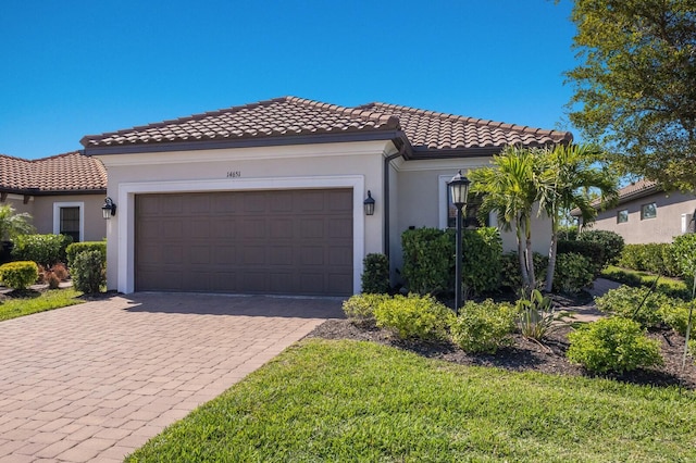 mediterranean / spanish-style home featuring stucco siding, an attached garage, a tile roof, and decorative driveway