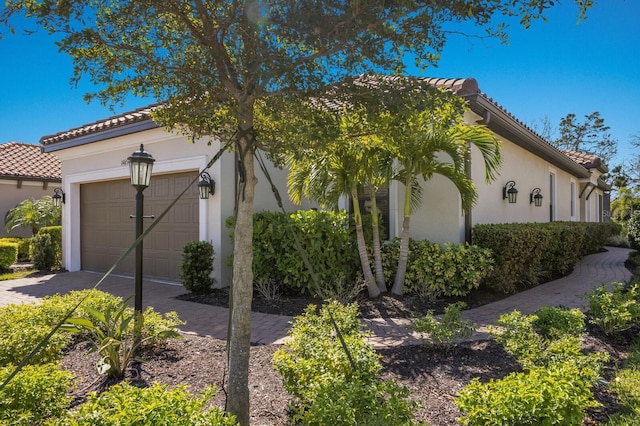 view of side of home with stucco siding, a garage, driveway, and a tiled roof