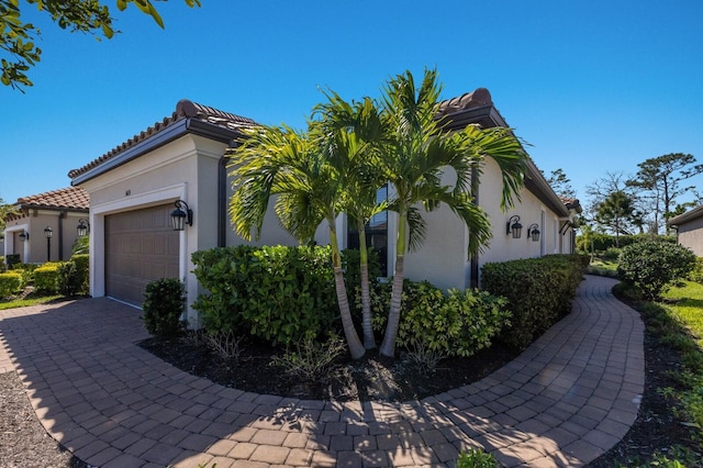 view of side of property featuring stucco siding, a tile roof, decorative driveway, and a garage