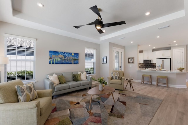 living area featuring ceiling fan, a raised ceiling, visible vents, and light wood-type flooring