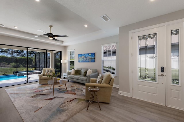 living area featuring visible vents, plenty of natural light, a raised ceiling, and wood finished floors