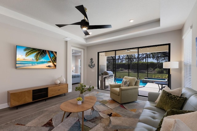 living room featuring baseboards, a raised ceiling, wood finished floors, and a ceiling fan